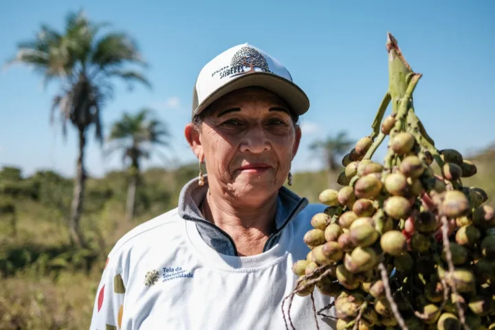 Mulher de boné segura um cacho de frutos da Caatinga, em Ibimirim (PE)